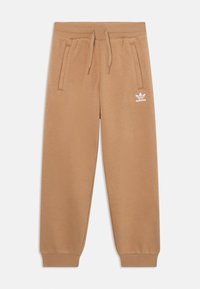 Sviestaini treniņbikses, izgatavotas no mīksta auduma, ar elastīgu jostu un aukliņām, sānu kabatām un baltu logo kreisajā augšstilbā.