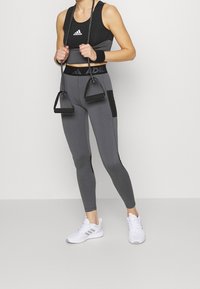Completo sportivo nero e grigio con top corto e leggings a vita alta. I leggings presentano dettagli neri e una texture liscia. Inclusi sneakers bianche.