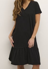 Czarna sukienka z dekoltem w serek, wykonana z miękkiego materiału, z krótkimi rękawami i rozkloszowanym, warstwowym falbanym dołem. Prosta, luźna sylwetka.