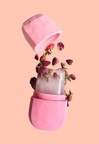 Stampo in silicone rosa per ghiaccio con un design geometrico, contenente un cubetto di ghiaccio trasparente con petali di rosa essiccati, circondato da petali sciolti.