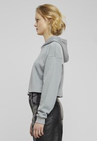 Felpa cropped grigia chiara con tasca frontale e cappuccio regolabile con cordino. Vestibilità rilassata con polsini a costine, indossata con pantaloni in pelle neri a vita alta.
