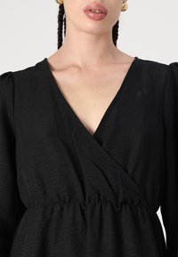 Melnas kleitas ar V veida kaklu, savilkta josta un garām pufojamām piedurknēm, izgatavotas no struktūrēta auduma, ar smalku spīdumu un plūstošu siluetu.