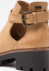 Bottine en cuir camel avec design découpé, boucle ajustable et semelle extérieure noire épaisse à crampons.