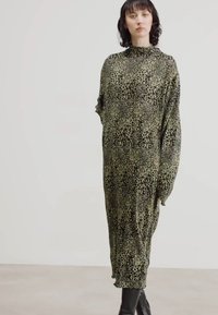 Robe longue et ample en vert olive avec un motif léopard noir. Tissu doux et col haut. Modèle associé à des bottes noires.