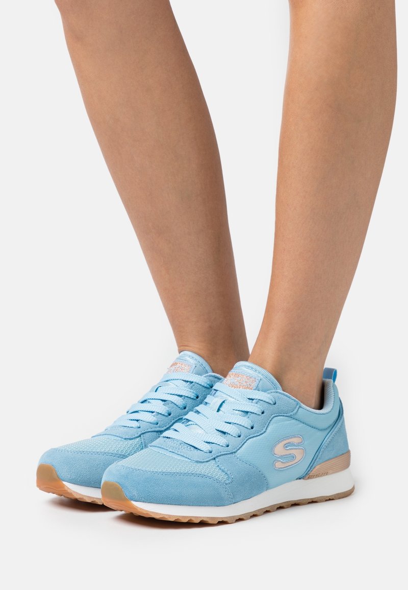 Baskets bleu clair à lacets avec semelles intermédiaires blanches et semelles en gomme, portées sur des jambes nues, vues de face et de côté.