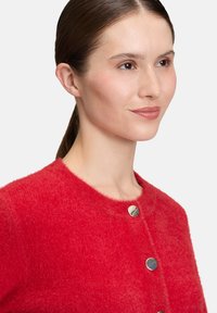 Czerwony, puszysty kardigan z okrągłym dekoltem i trzema srebrnymi guzikami z przodu. Miękka tekstura i luźny krój.