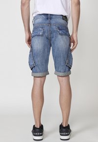 Leren denim cargoshorts in lichtblauw met omgeslagen cuffs, voorzien van meerdere zijzakken en een vervaagde textuur, gecombineerd met zwarte sneakers.