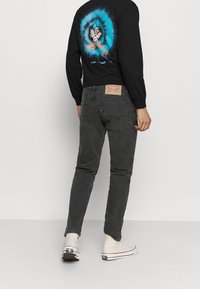 Persona con sudadera negra con un diseño de personaje de anime azul, jeans gris oscuro y zapatillas blancas de caña alta, de espaldas.