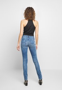 Blå skinny jeans med bakfickor och ett vågmönster, i kombination med en svart ärmlös topp. Slät denimtextur, figurnära passform.