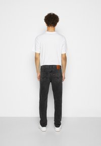 Sorte denimjeans med rett snitt og teksturert overflate. Har to baklommer og en brun lærmerkelapp på livet. Hvit T-skjorte.