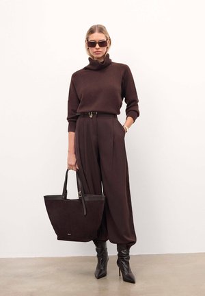 Brauner Strickpullover mit hohem Kragen, weit geschnittene braune Hose, schwarze Stiefeletten mit Absatz und eine strukturierte braune Wildleder-Handtasche.