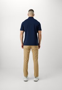 Polo à manches courtes navy, associé à un pantalon beige et des baskets blanches. Tissu lisse avec une coupe classique et un détail de col subtil.