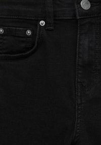 Gros plan d’un jean en denim noir montrant la poche avant, la boucle de ceinture, le bouton et les rivets avec les détails de couture visibles.
