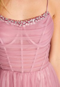 Roze jurk met een getailleerde lijfje en gelaagd nettextuur, voorzien van een met juwelen versierde halslijn met roze en heldere kralen.