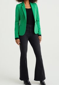 Grön blazer med en skräddarsydd design, matchad med svarta utsvängda jeans. Tyget ser slätt ut och blazern har en enkel knappstängning.