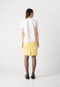 White short-sleeve top and yellow skirt with a back slit, paired with black shoes and sheer black tights. Simple design, smooth textures.