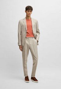 Light beige plaid suit with matching trousers; coral t-shirt underneath; brown shoes; smooth fabric; fitted design; casual yet tailored look.