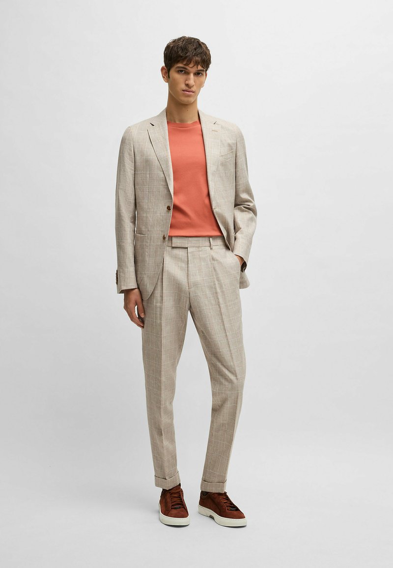 Light beige plaid suit with matching trousers; coral t-shirt underneath; brown shoes; smooth fabric; fitted design; casual yet tailored look.