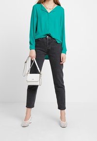 Blusa turchese con scollo a V, jeans neri a gamba dritta, borsa bianca e scarpe intrecciate bianche. Tessuto morbido e design semplice.