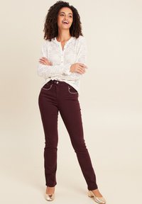 Blouse en dentelle avec un devant à boutons, manches longues et motif floral ; jeans bordeaux ajustés avec des coutures argentées et longueur cheville ; talons dorés.