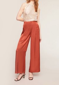 Satin, högmidjade, rostfärgade byxor med vida ben och framveck; matchade med en paljett-topp och svarta sandaler.