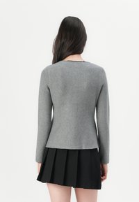 Grå langermet topp med tettsittende design, rund halsringning og myk tekstur, kombinert med et svart plisséskjørt. En enkel og minimal estetikk.