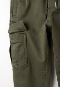 Olijfgroene cargobroek van dik materiaal, met een zijzak, verstevigde stiksels en een taille met trekkoord en metalen accenten.