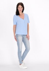 Svetlo modrý krátky cardigan s V-výstrihom, textúrovaným rebrovým dizajnom a predným zapínaním na gombíky. V kombinácii so svetlo modrými skinny džínami a bielymi teniskami.