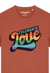 T-shirt couleur rouille avec un col rond et des manches courtes, arborant "CÉLÉBREZ L'AMOUR" en lettres majuscules multicolores.