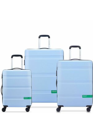 Tres maletas rígidas de color azul claro, de diferentes tamaños. Cada una presenta surcos horizontales y detalles de marca en verde. Con asas retráctiles y ruedas.