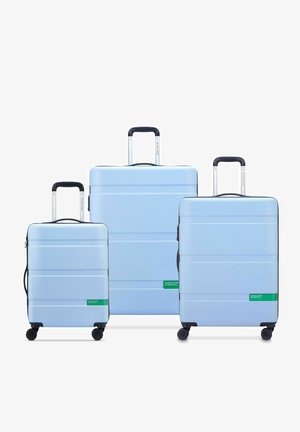 Tre valigie rigide di colore azzurro, di diverse dimensioni. Ognuna presenta scanalature orizzontali e dettagli di branding verdi. Manici estraibili e ruote.
