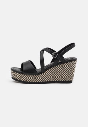Black leather wedge sandals with cross straps, featuring a herringbone-patterned woven platform and adjustable ankle strap.