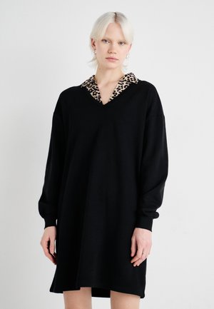 Svart oversized kjole med lange ermer og v-hals, med en leopardmønstret krage. Laget av et mykt, teksturert stoff.