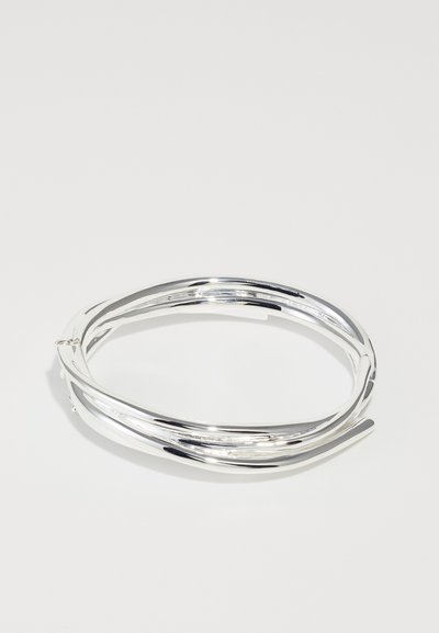 Sølv metalarmbånd med sammenflettet design, glat overflade og poleret finish. Har en tynd, fleksibel struktur for en tæt pasform.