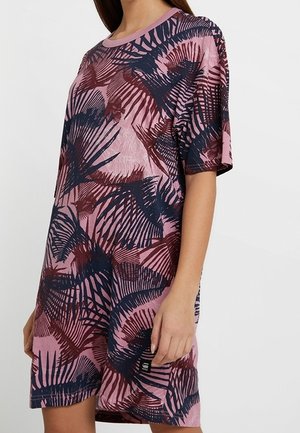 Kobieta w luźnej różowej sukience z abstrakcyjnymi wzorami liści w kolorach granatowym i bordowym, z krótkimi rękawami i okrągłym dekoltem.
