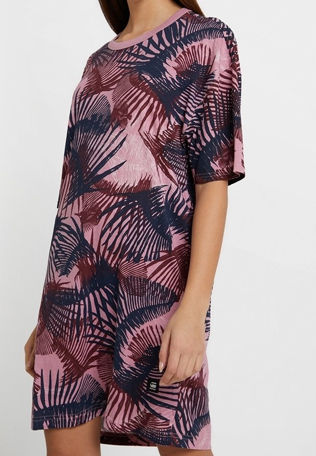 Femme portant une robe ample rose avec des motifs abstraits de feuilles bleu marine et bordeaux, manches courtes et encolure ronde.