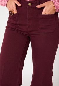 Pantaloni a vita alta bordeaux realizzati in misto cotone, con due tasche frontali, chiusura a bottone e dettagli di cucitura sottili.
