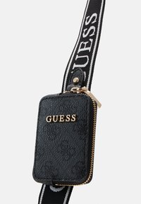 Čierna textúrovaná kožená taštička so zlatým logom "GUESS", obsahujúca zlatý zips, pripojená k čierno-bielemu označenému remienku.