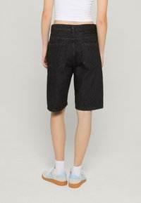 Shorts en denim noir avec une coupe ample, arrivant au milieu de la cuisse, dotés de deux poches arrière et d'une taille avec logo. Style décontracté avec un design simple.
