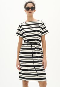 Abito a righe in bianco e nero con maniche corte, vestibilità comoda, vita cintrata e cintura da annodare. Tessuto liscio con righe a contrasto.
