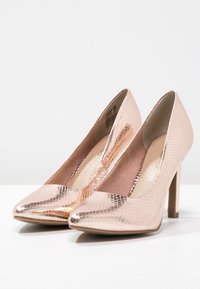 Décolleté occhi di gatto in oro rosa con motivo a serpente texturizzato, punta affusolata e tacco sottile e slanciato. Fodera interna morbida.