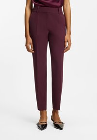 Burgundy tailored trousers with a high waist, featuring sharp creases, smooth texture, and side zip accents for a sleek fit.