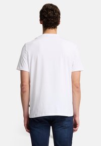 Hvid t-shirt med korte ærmer og rund halsudskæring, glat tekstur og afslappet pasform, kombineret med mørkeblå denimjeans.