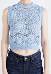 Ljust blå virkad crop top med vågiga kanter och ett honungscombmönster. Stylad med mörka denim jeans med hög midja.