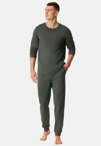 Conjunto de ropa de casa en verde oscuro que incluye una camiseta de manga larga con un bolsillo texturizado y pantalones ajustados a juego con puños elásticos, fabricado en un tejido suave.