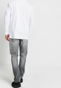 Camisa blanca de manga larga con corte recto, combinada con vaqueros grises descoloridos y zapatos negros. Costuras traseras y bolsillos visibles en los vaqueros.