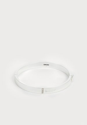 Balta metāla rokassprādze ar gludu virsmu, iegravētu logo un trim mazām caurspīdīgām akmeņiem kā akcents. Aiztaisāma dizaina.