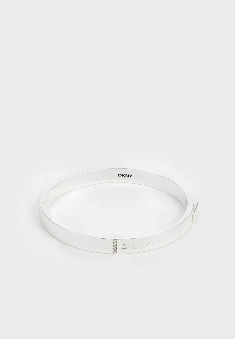 Valge metallist käevõru, millel on sile viimistlus, graveeritud logo ja kolm väikest selget kivi aksessuaaridena. Suletud disain.