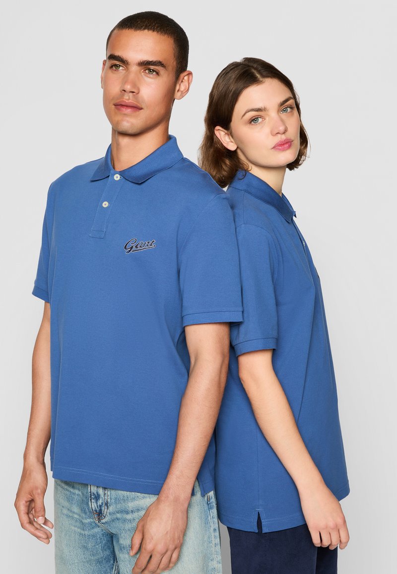 Chemises polo bleues en coton, dotées d'un col et de manches courtes. Chacune a un logo brodé sur la poitrine et des fentes sur les côtés à l'ourlet.