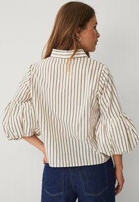 White shirt with vertical brown stripes, puffed sleeves, and a structured collar. Fabric appears smooth with a relaxed fit at the back.